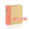A coral-colored binder with a limited edition label on the front, featuring a snap closure.